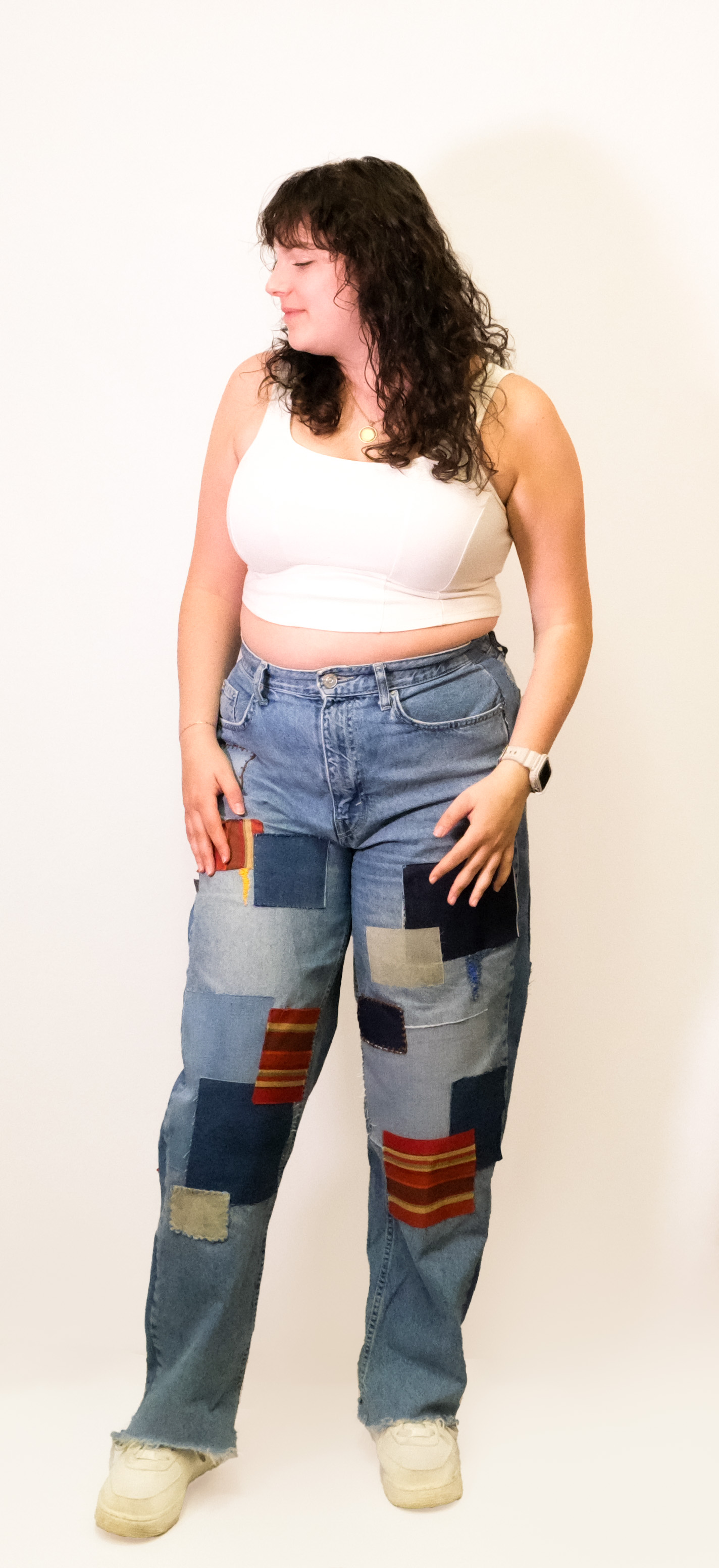 A model wears patchwork denim jeans pieced from multicolored fabric squares and a white tank top.