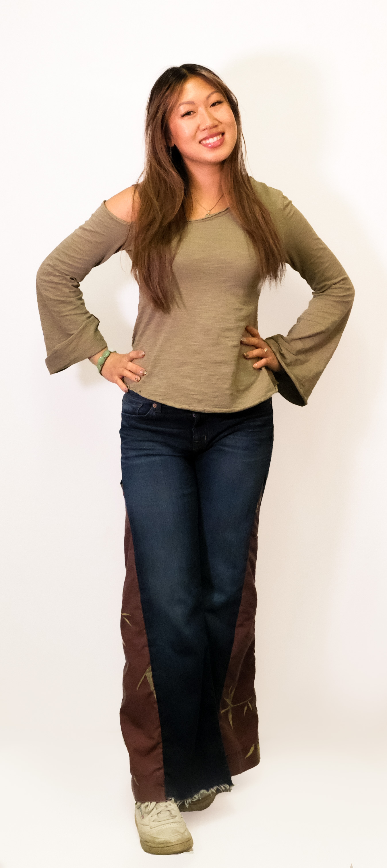 A smiling model in a bell-sleeve top and dark flared jeans with brown side panels.