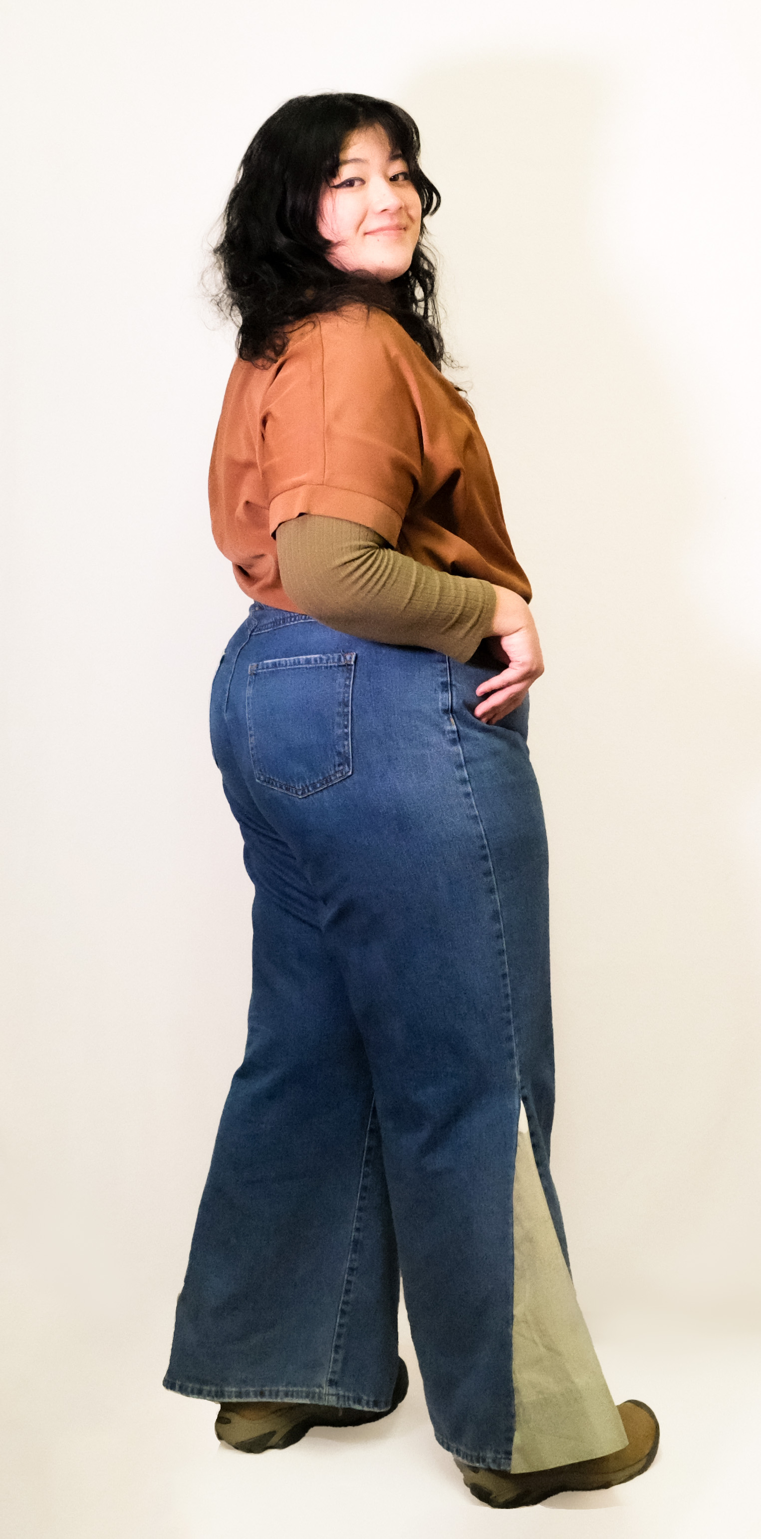A model shown from behind in wide-leg jeans with a tan side gusset, smiling over her shoulder.