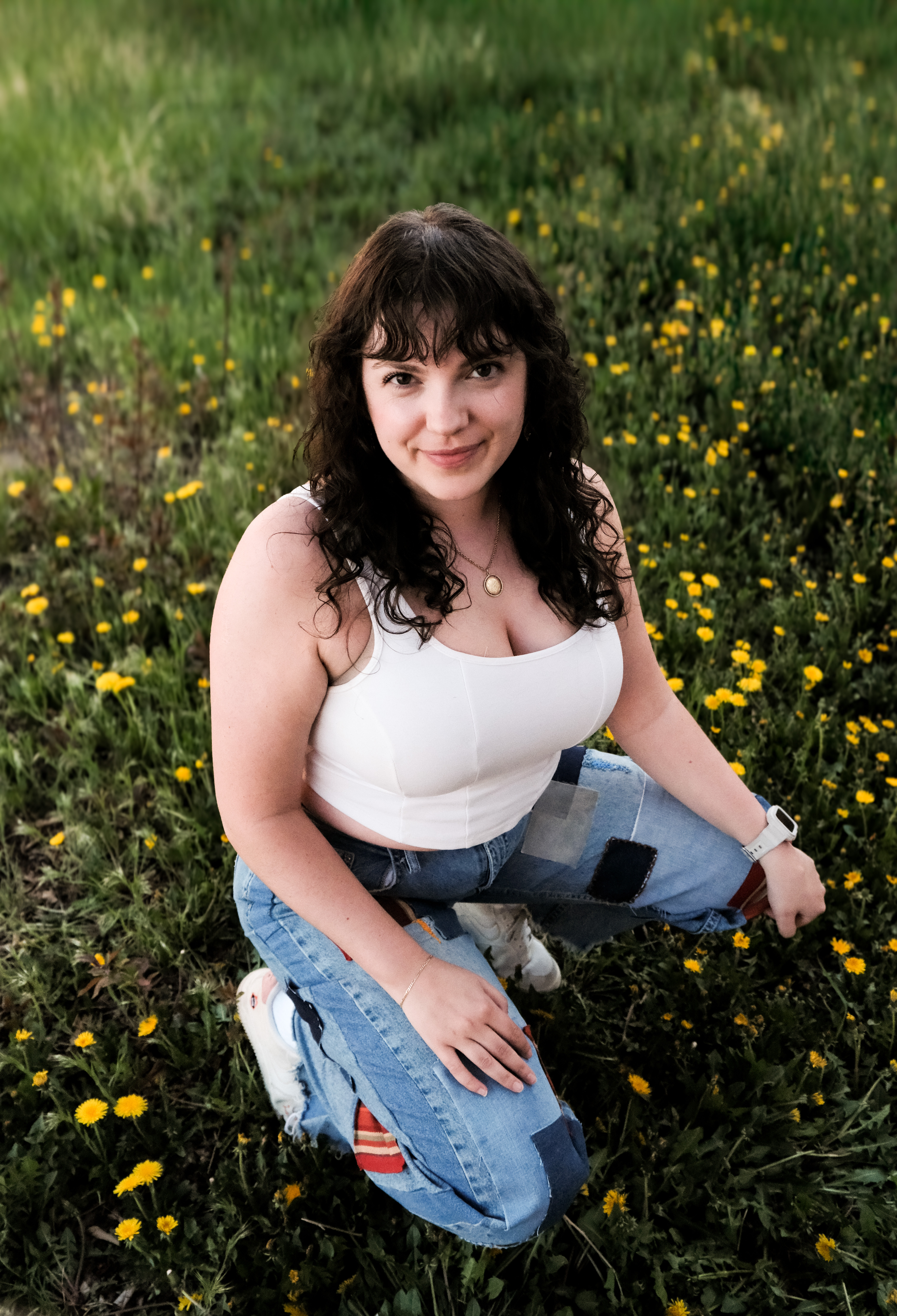 A model in patchwork denim jeans and a white tank top crouches in a field of dandelions.