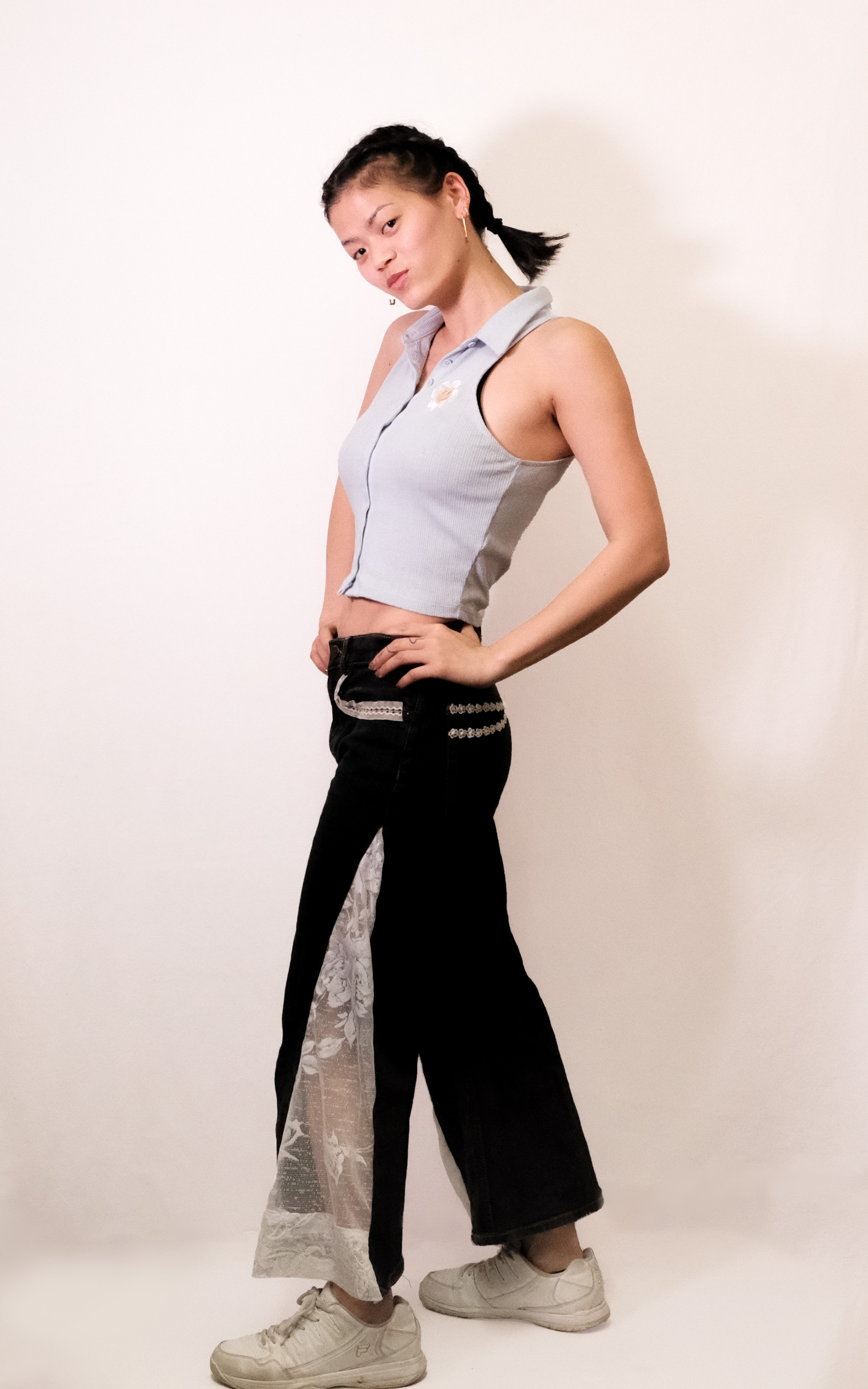 A model in a sleeveless blue collared top and black flared pants with a lace inset panel.