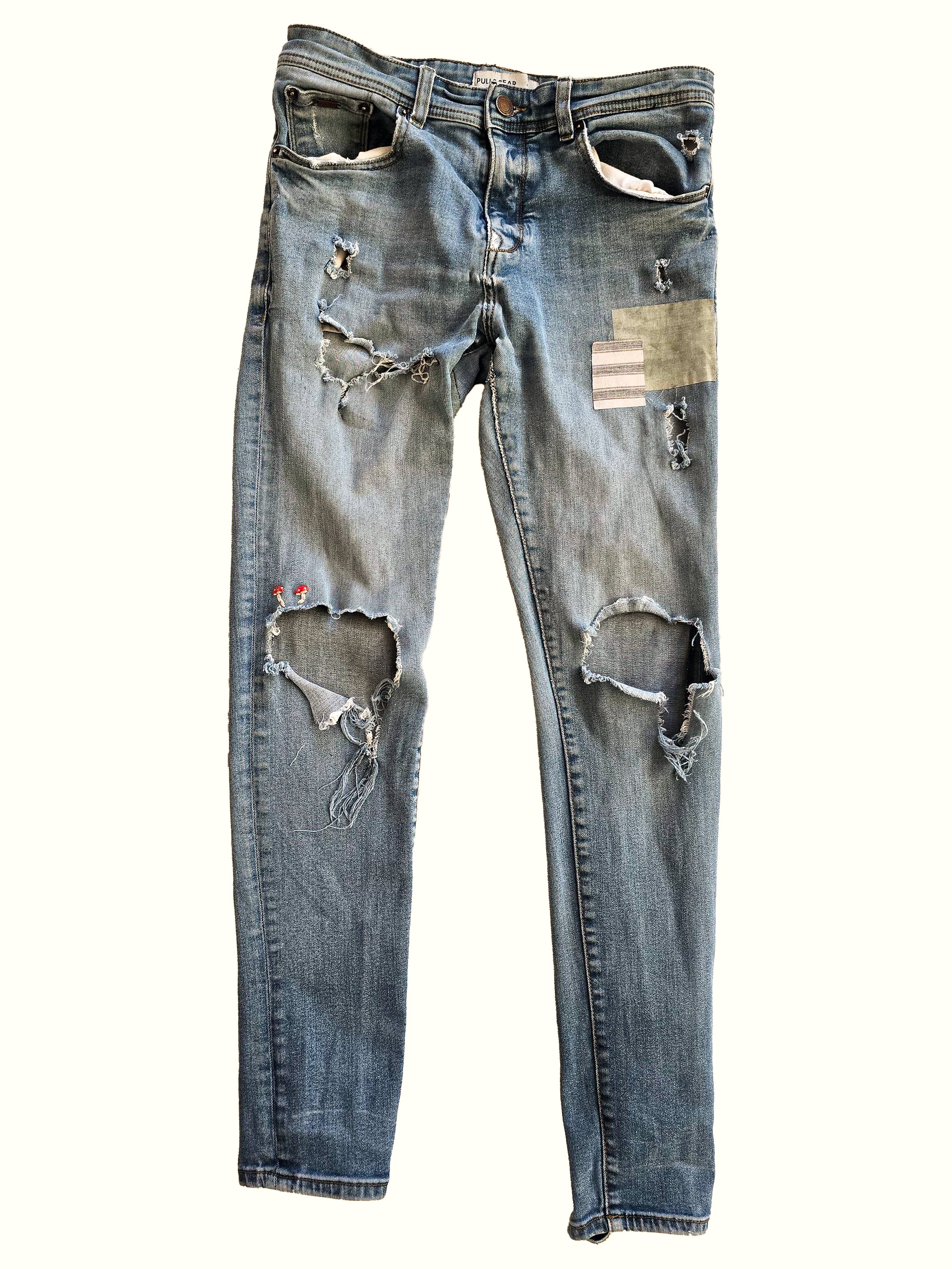 Flat-lay of distressed light-wash jeans with knee rips, a sewn patch, and embroidered details.