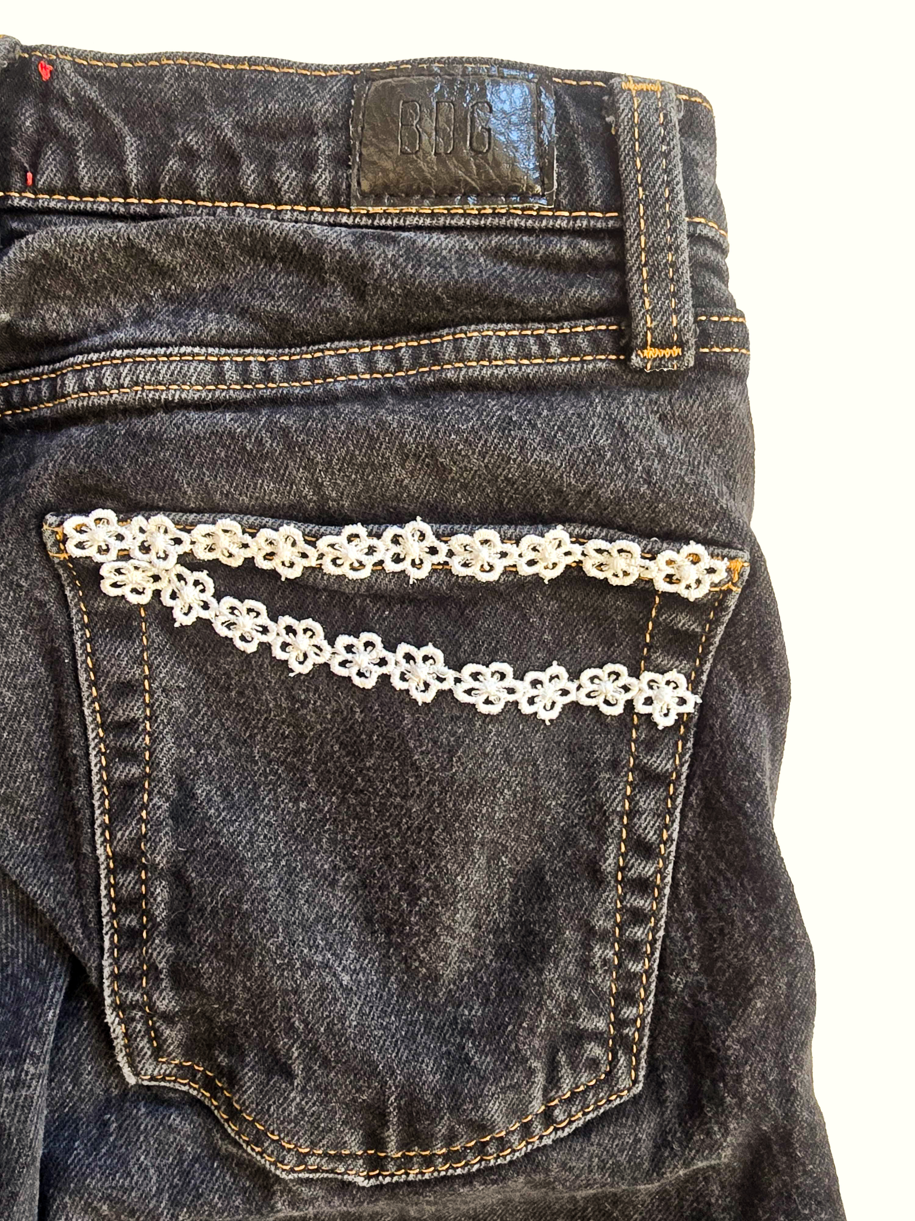 Close-up of a dark jeans back pocket trimmed with white floral lace ribbon.