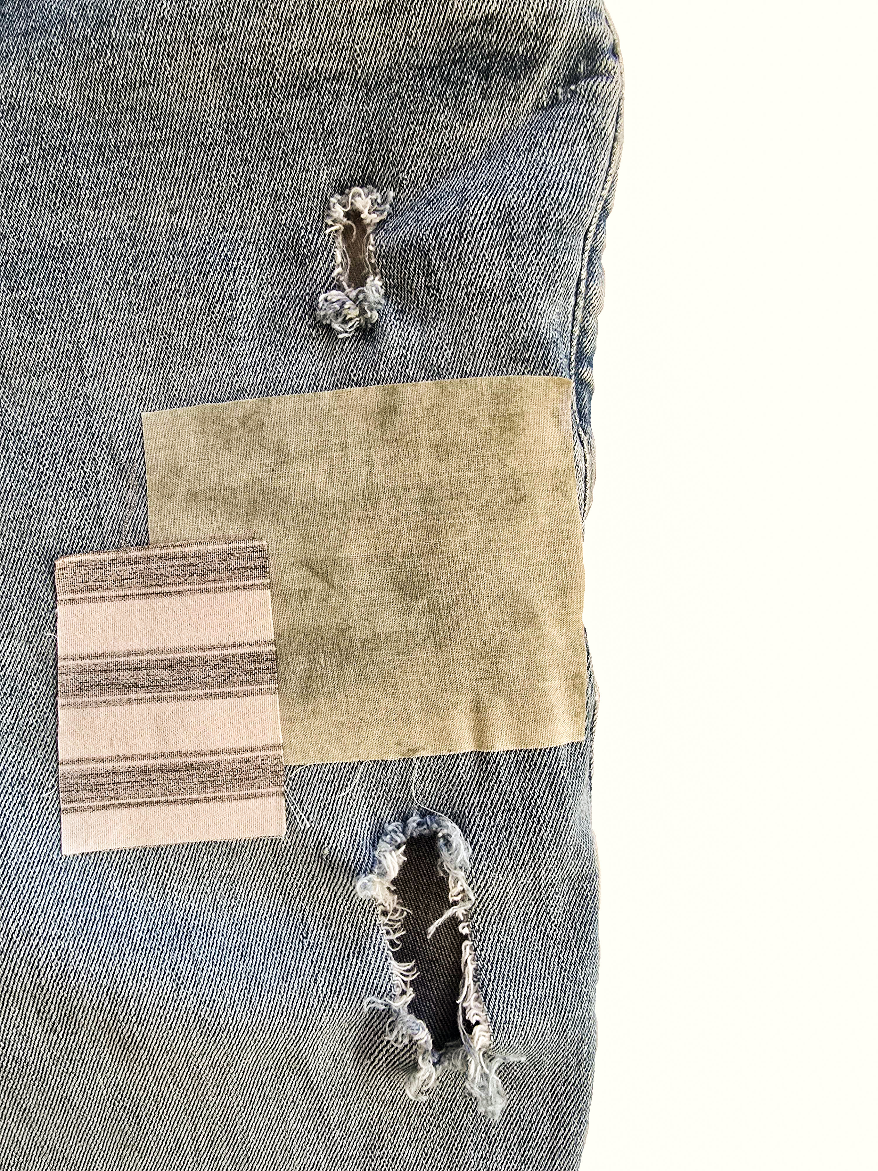 Close-up of light jeans with olive and striped fabric patches sewn over distressed holes.