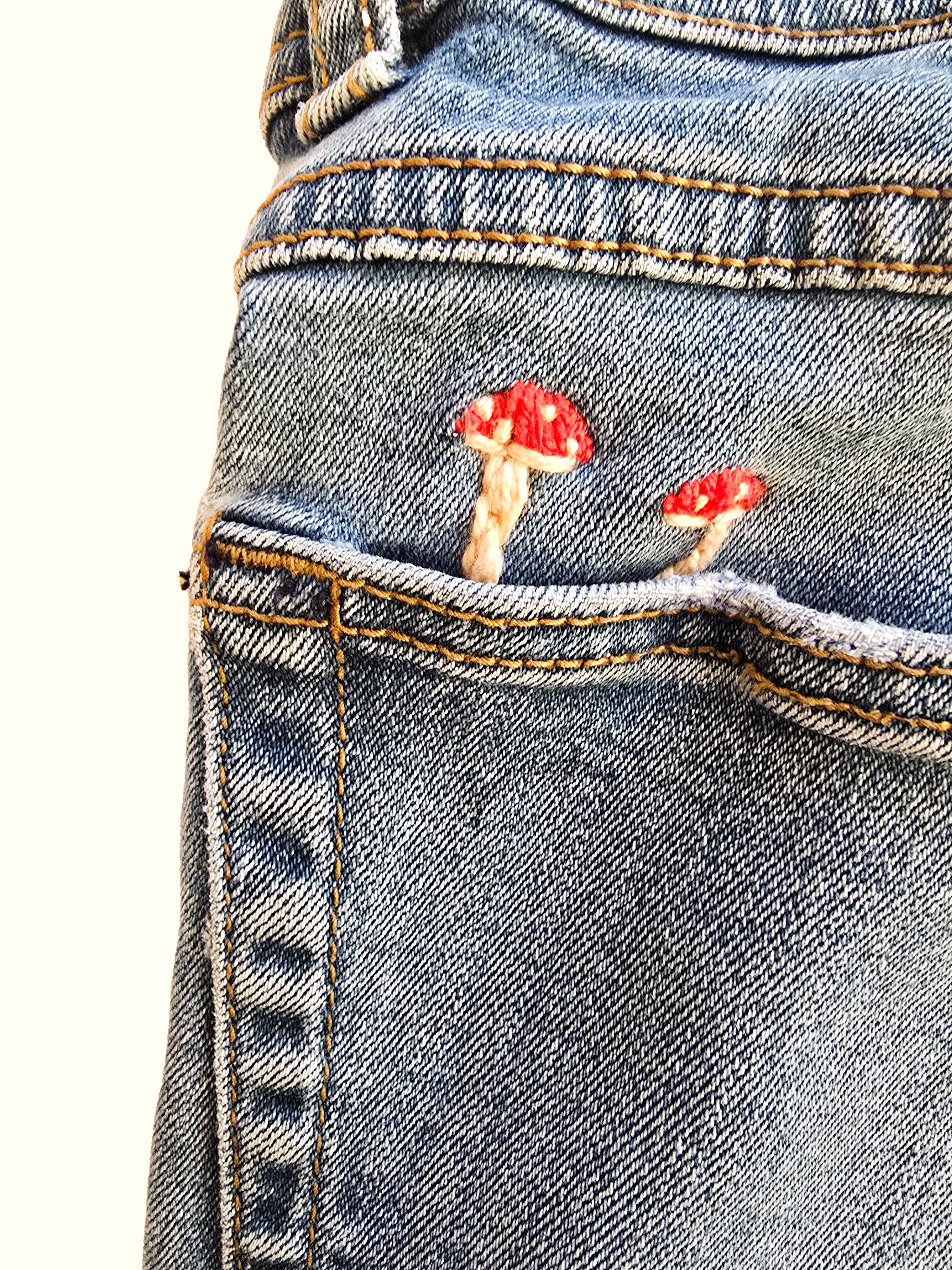 Close-up of red embroidered mushrooms stitched onto a denim pocket.