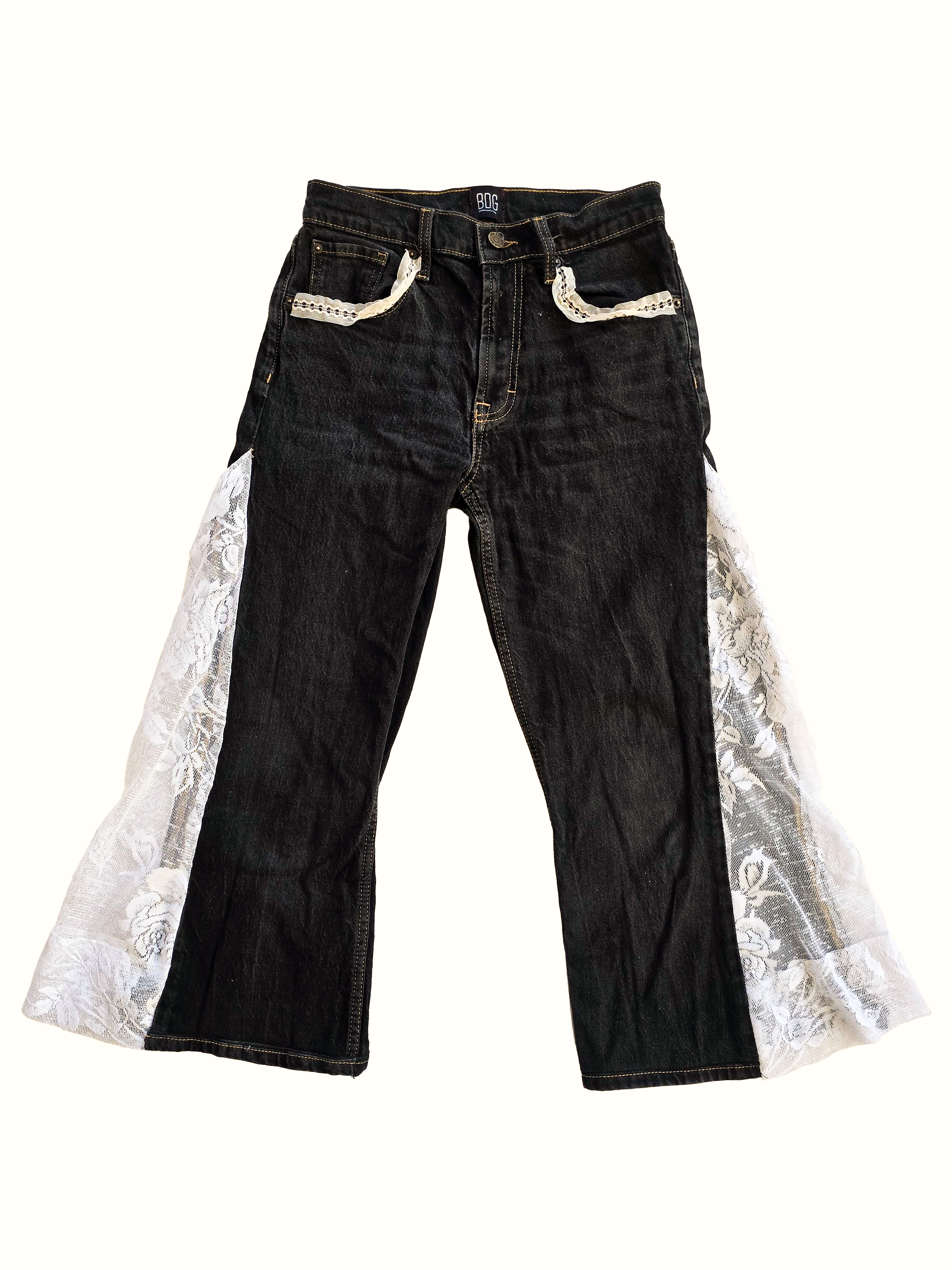 Flat-lay of black flared jeans with white floral lace side panels and lace pocket trim.