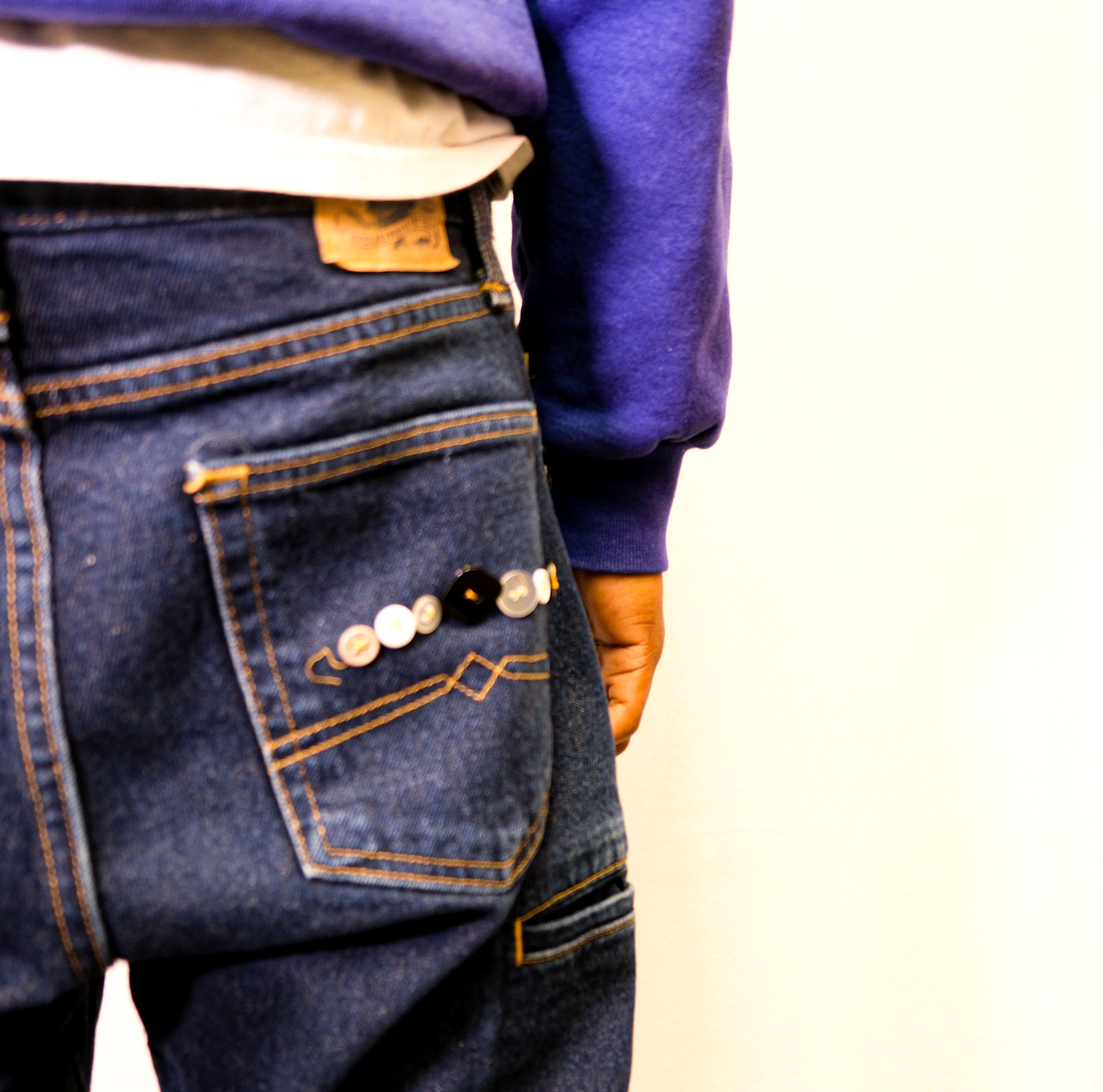Close-up of a dark jeans back pocket decorated with a row of assorted sewn-on buttons.