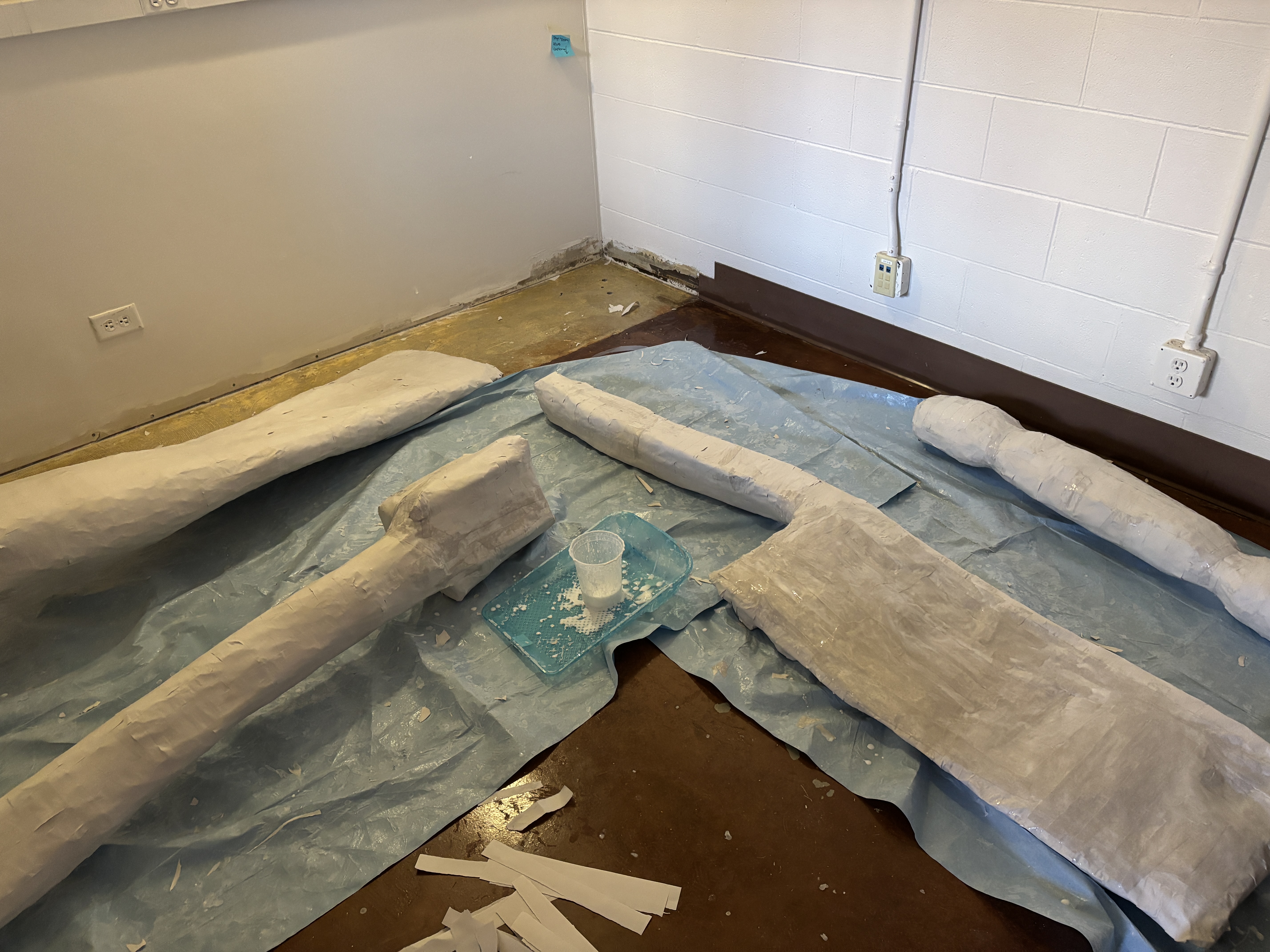 Large white plaster forms under construction on the floor of a workspace with blue drop cloths.