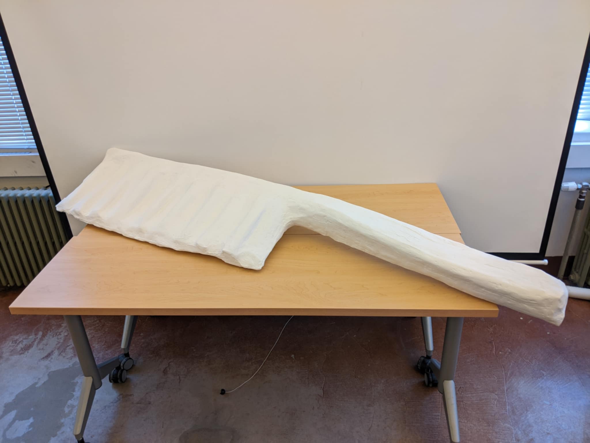 A long white plaster sculpture of an oversized comb with ridged teeth, on a wooden table.