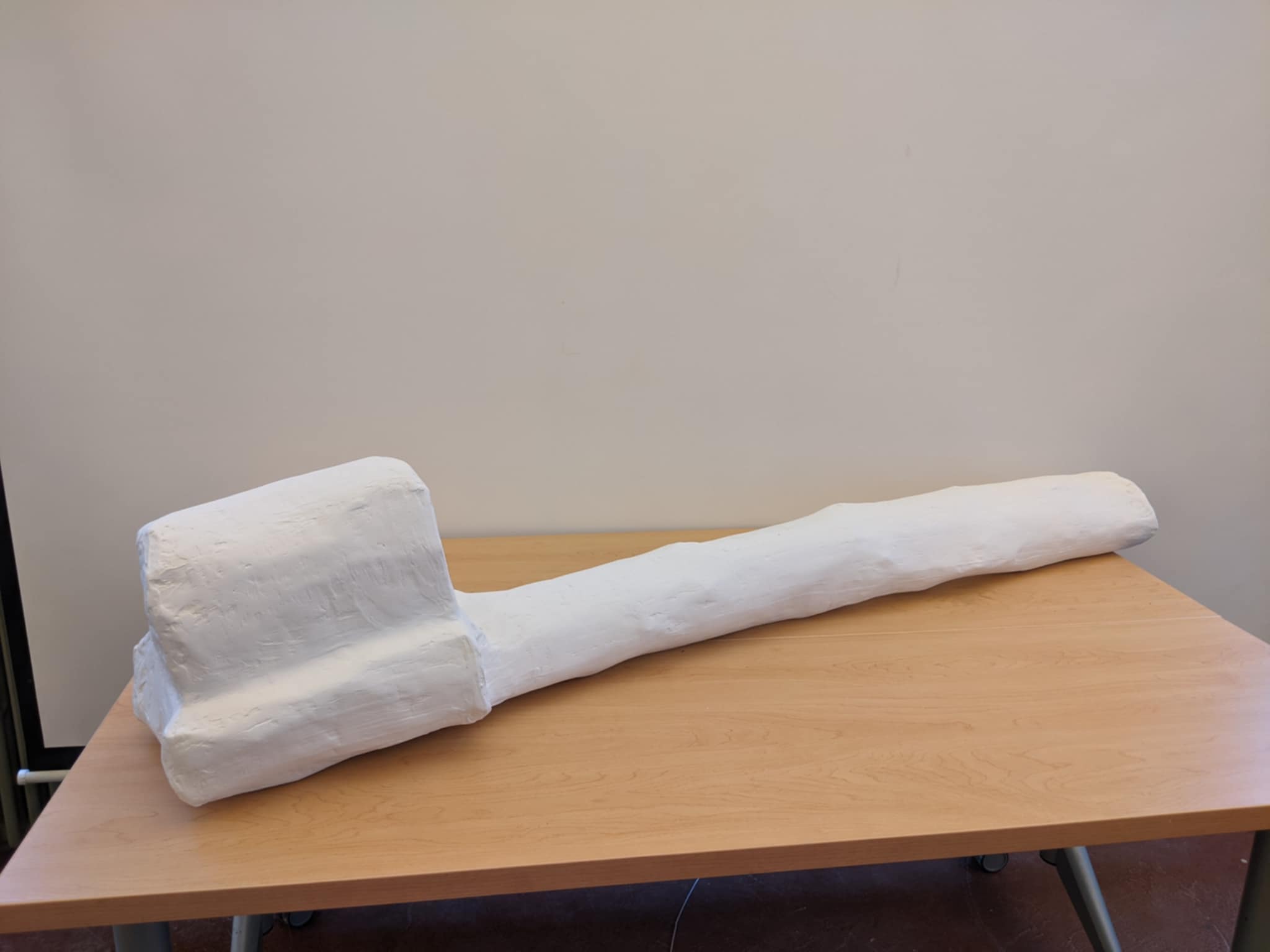 A large white plaster sculpture of an oversized toothbrush resting on a wooden table.
