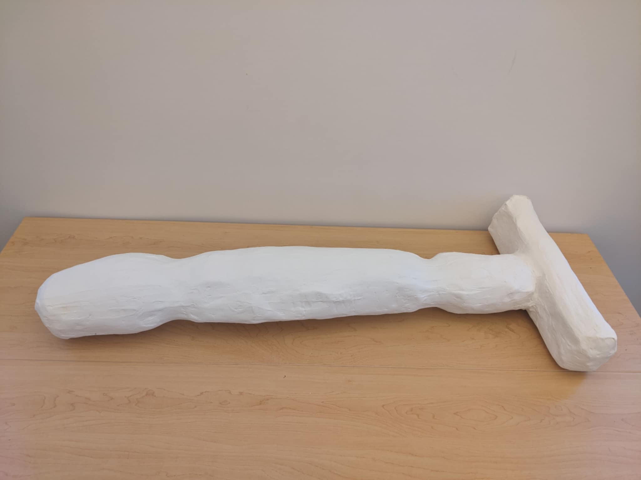 A large white plaster sculpture of an oversized razor lying on a wooden table.