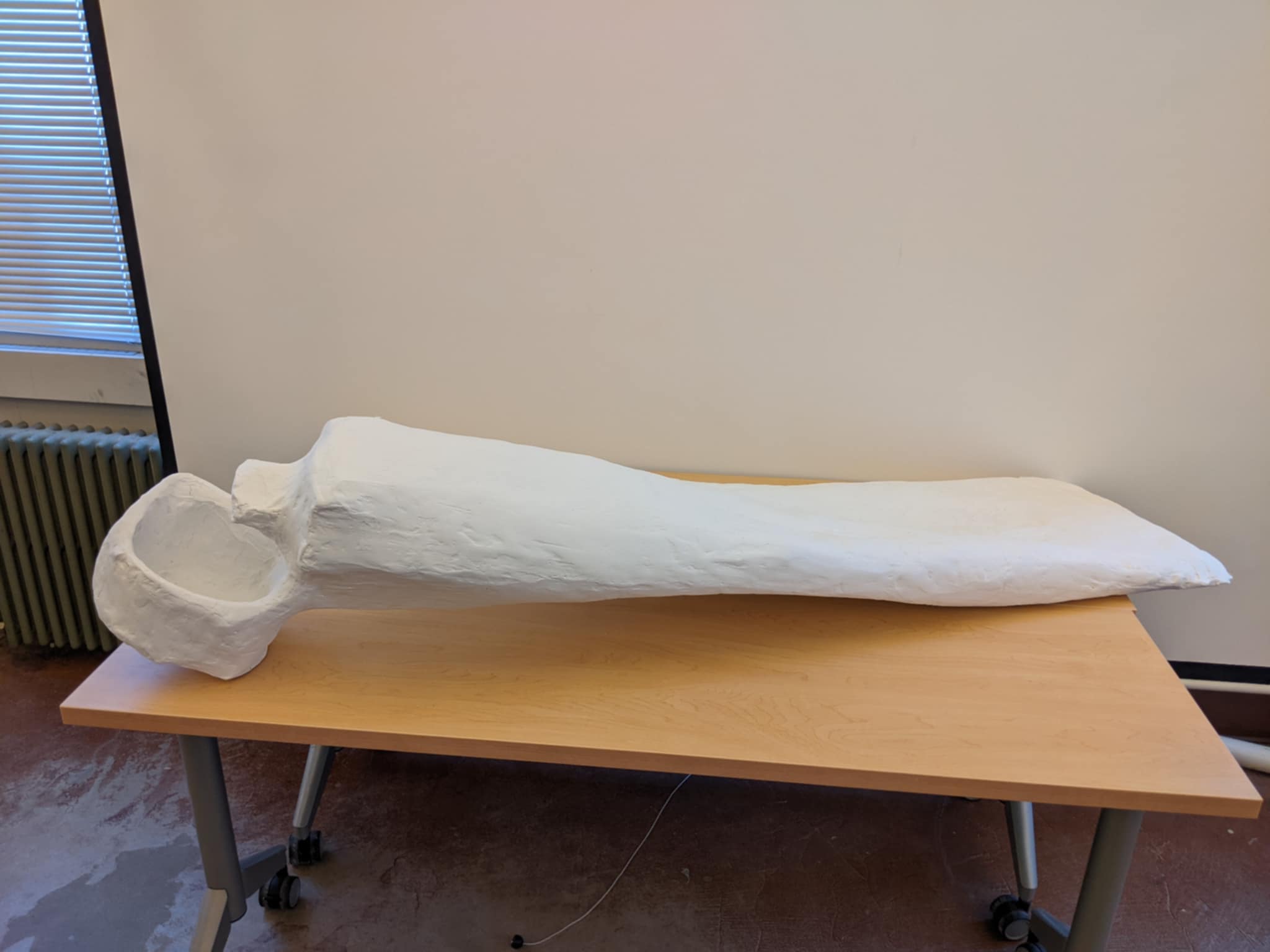A large white plaster sculpture of an oversized toothpaste tube on a wooden table.