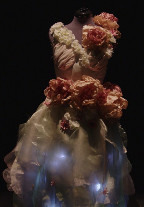 Mannequin gown of fabric flowers and sheer skirt glowing with embedded blue LEDs in the dark.