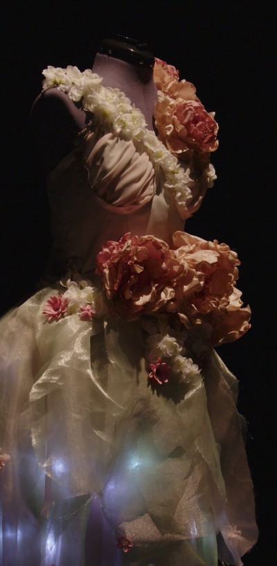 Angled view of the floral LED gown, peony blooms over a luminous sheer skirt on a mannequin.