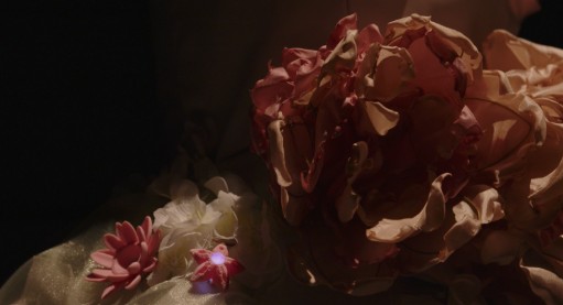 Close-up of dried-looking fabric peonies with a small glowing blue LED among the petals.