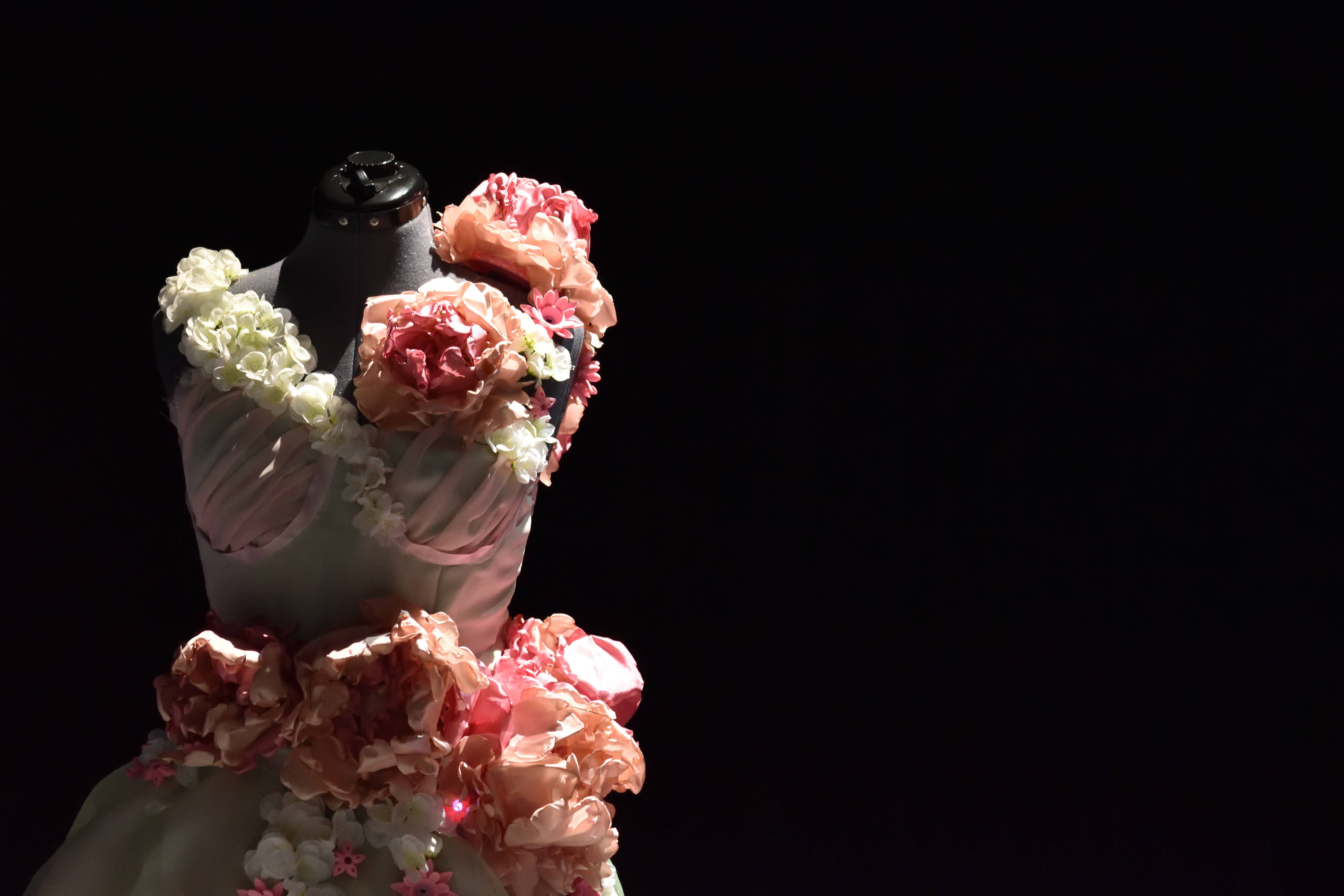 Spotlit floral gown on a mannequin, fabric peonies and hydrangeas across the bodice and skirt.